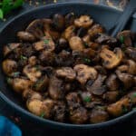 Sauteed Mushroom in a dark grey bowl with few ingredients scattered around.