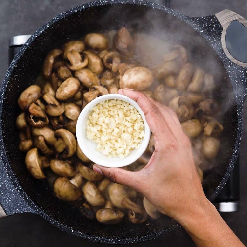 Adding garlic to the pan with mushroom.