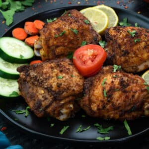 Air Fryer Chicken Thighs in a black plate with few ingredients scattered around.