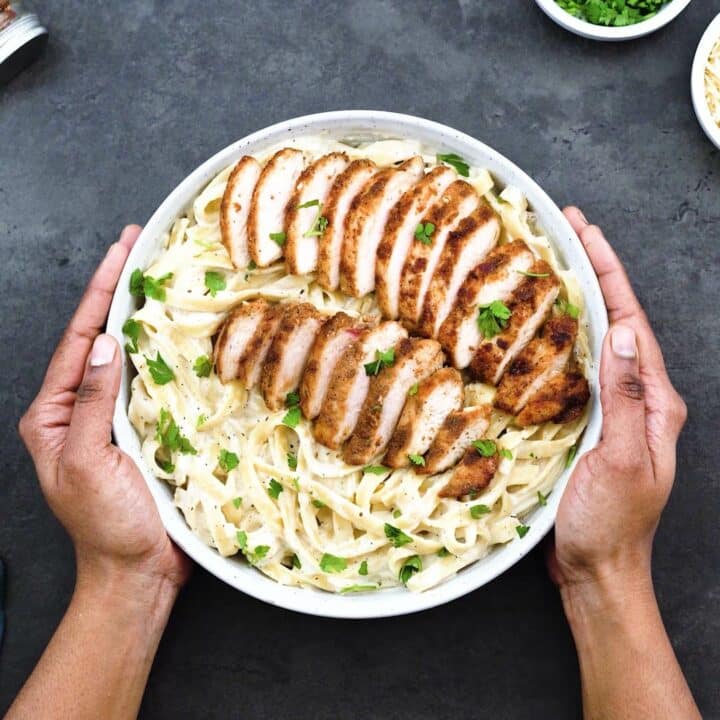 Serving Alfredo Pasta topped with chicken breast in a white bowl.