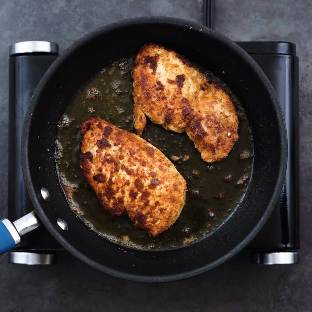 Chicken breast being fried in a pan.