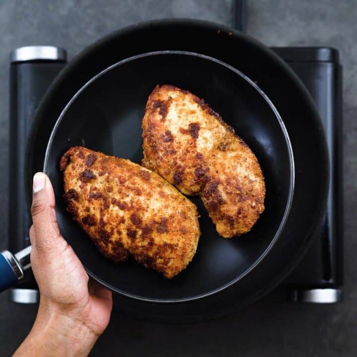 Pan fried chicken breast on a black plate.