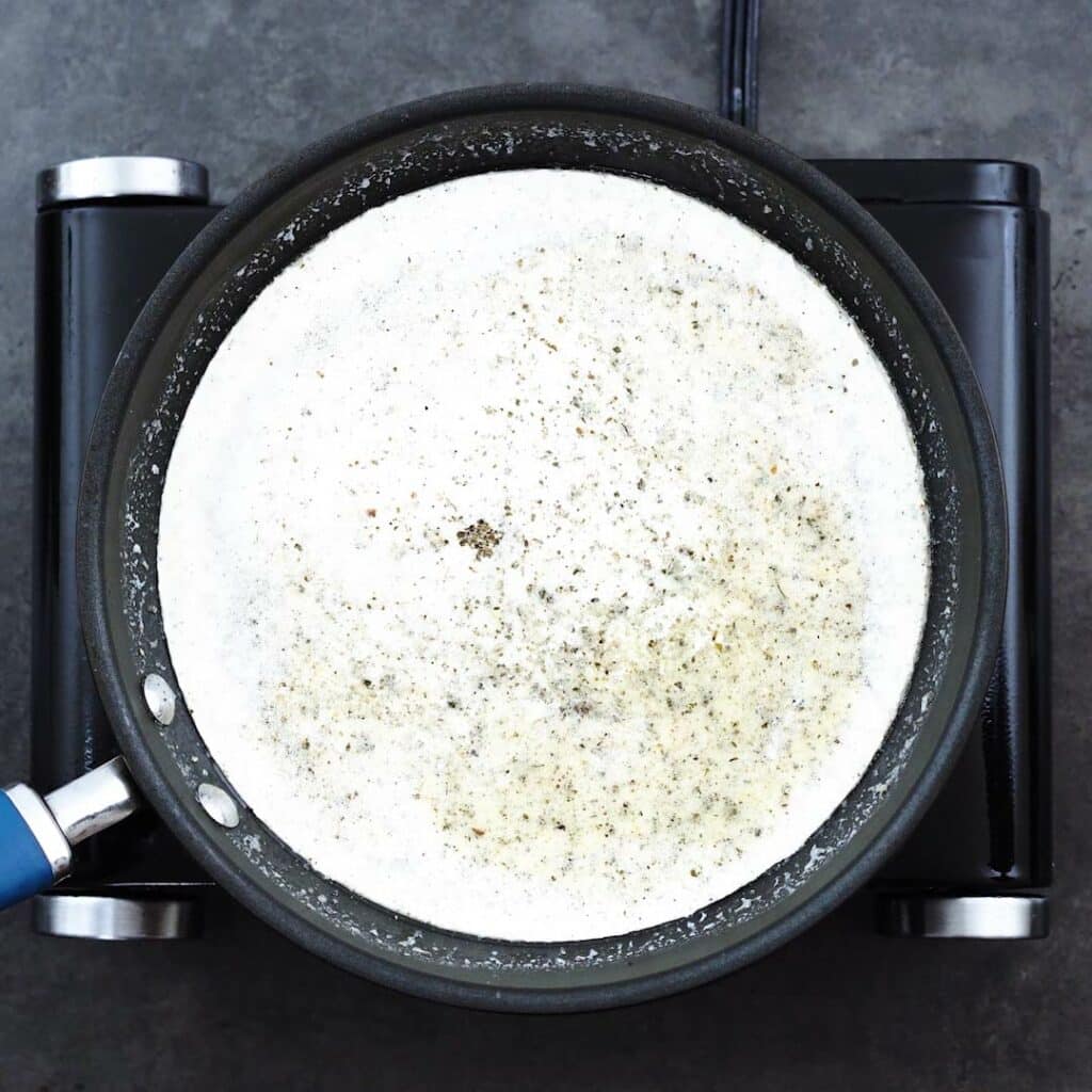 Seasoned heavy cream simmering in a pan.