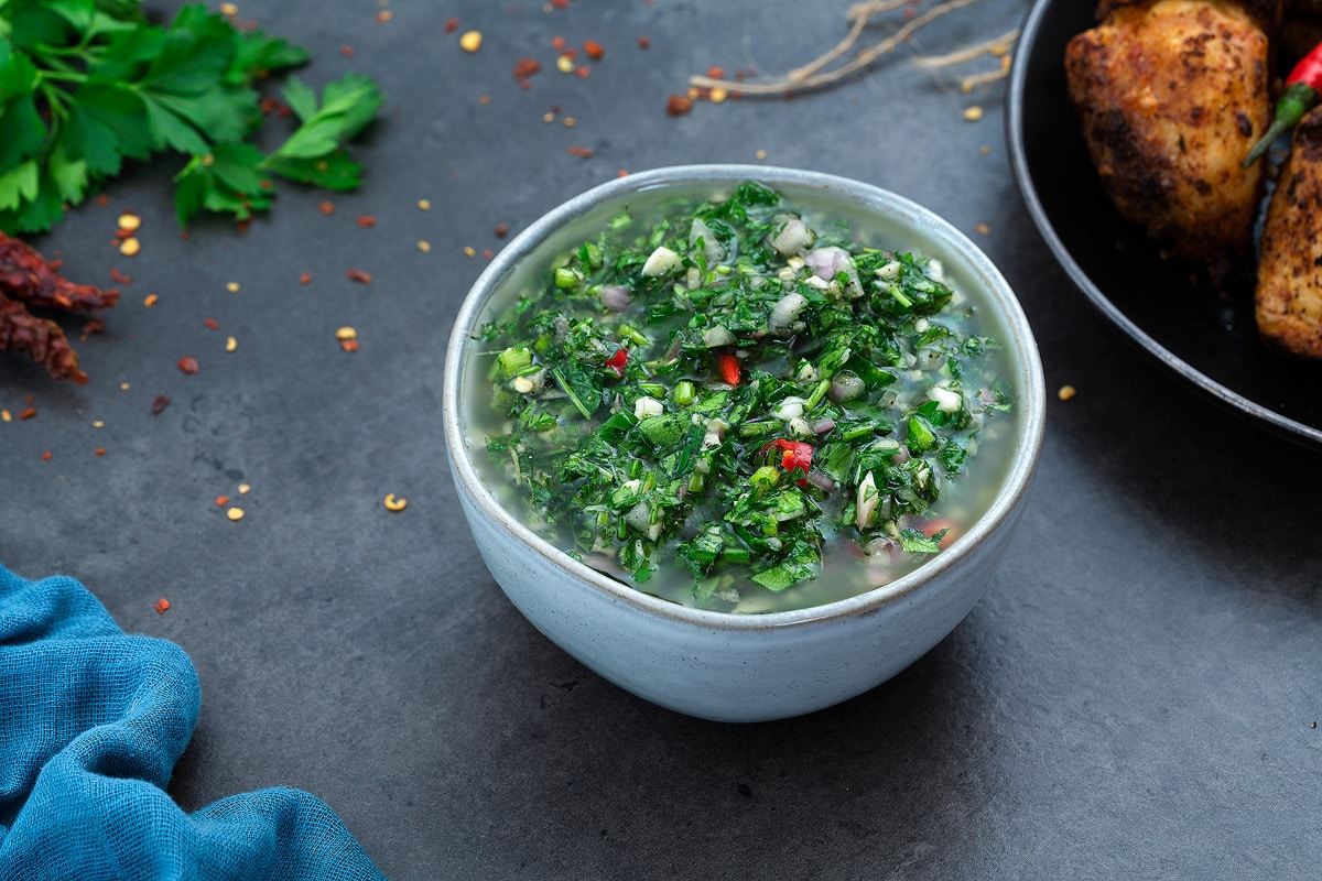 Chimichurri Sauce in white bowl with few ingredients scattered around.