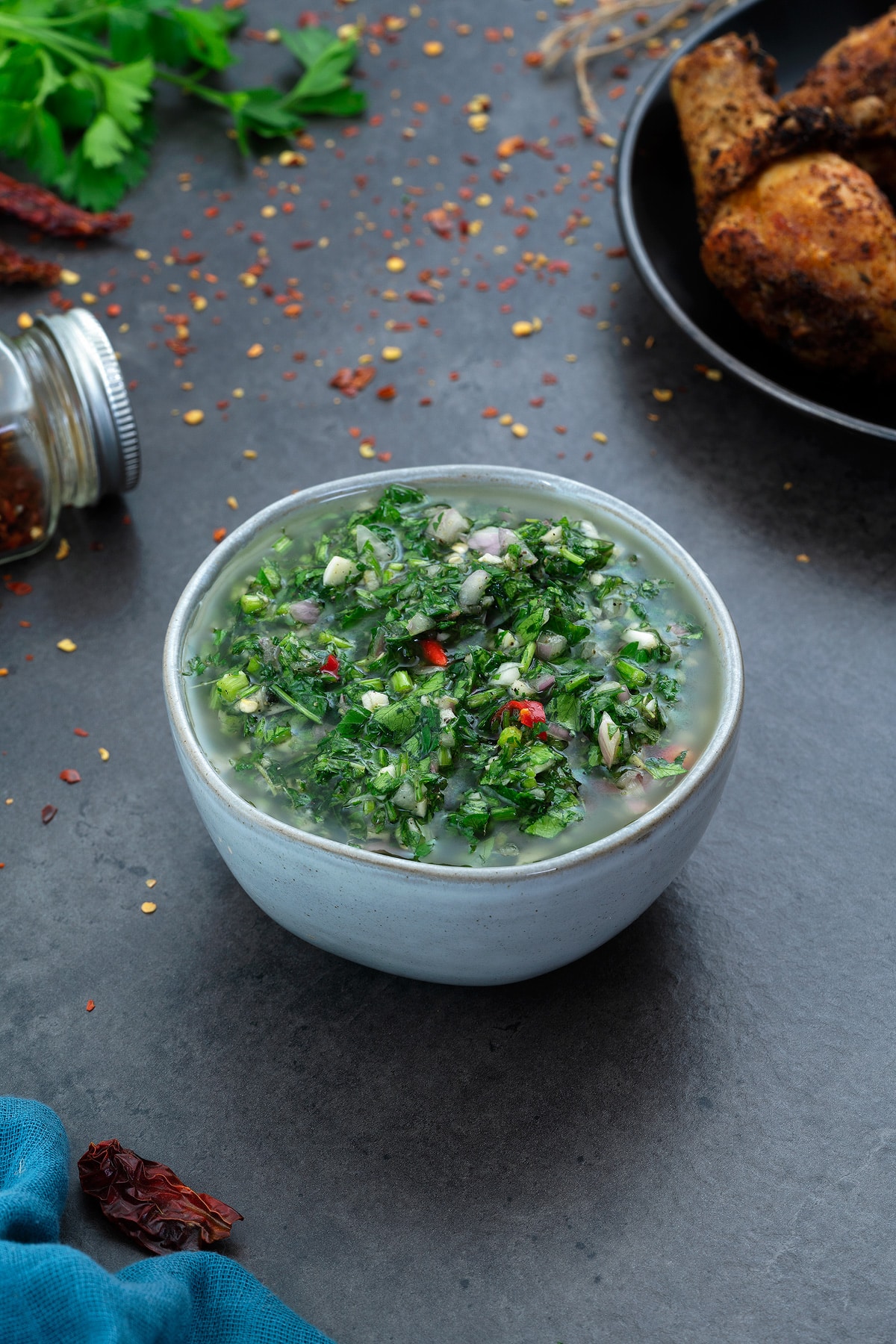Chimichurri Sauce in white bowl with few ingredients scattered around.