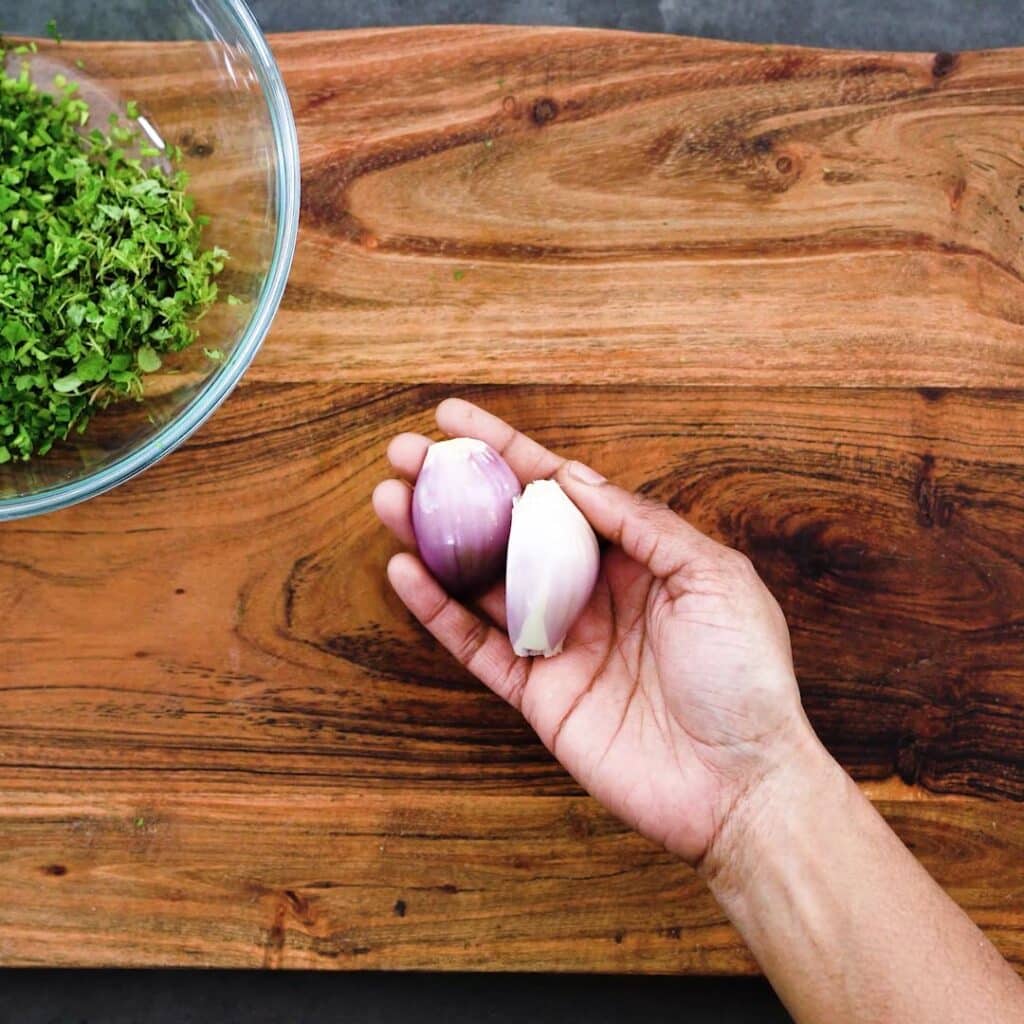 An overhead view of a hand holding shallots above a wooden cutting board.