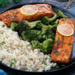 Baked Salmon fillets in a black plate with brown rice and broccoli.
