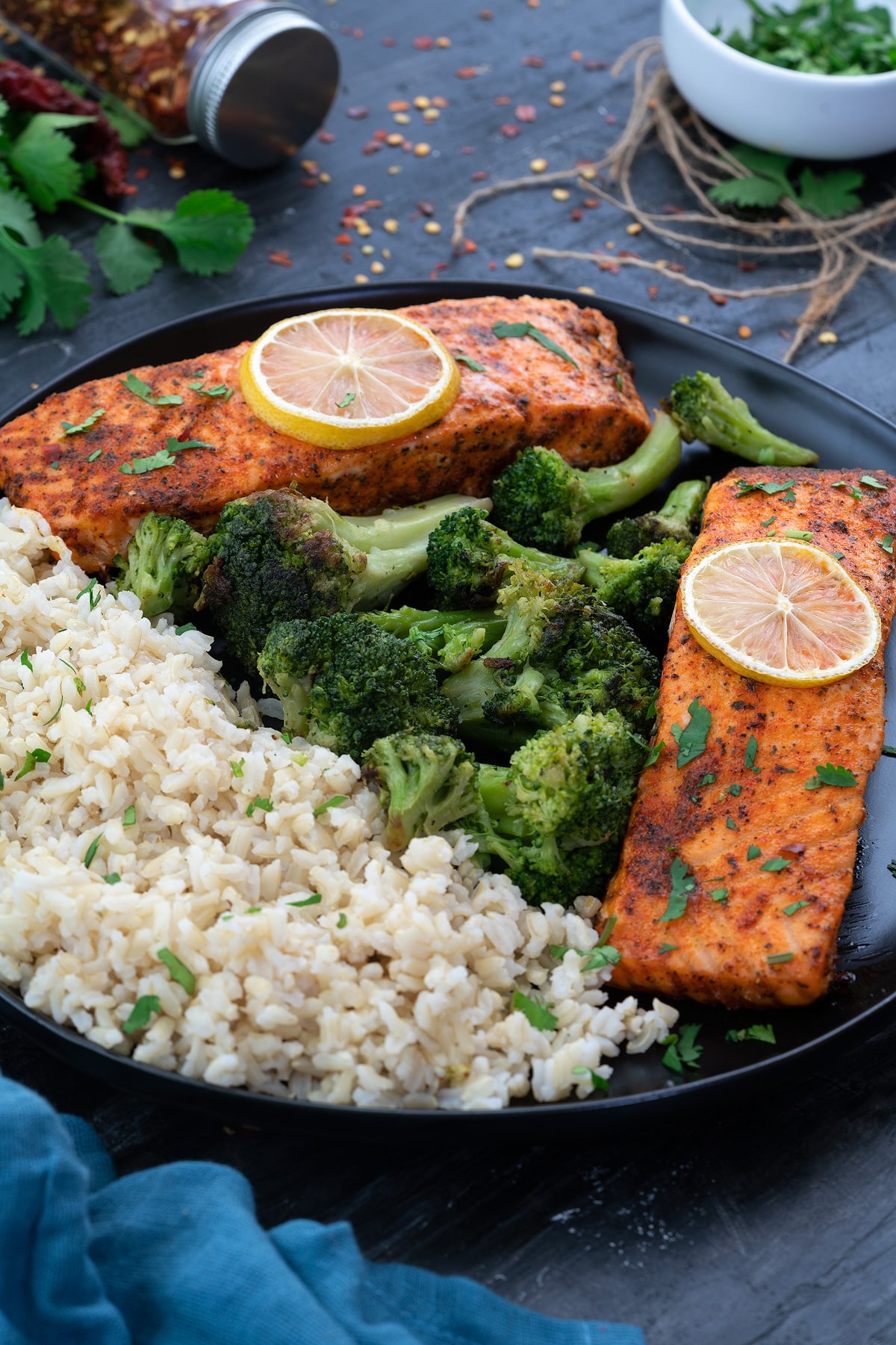 Baked Salmon fillets in a black plate with brown rice and brocolli.