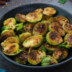 Sauteed Brussel Sprouts in a black bowl with few ingredients scattered around.