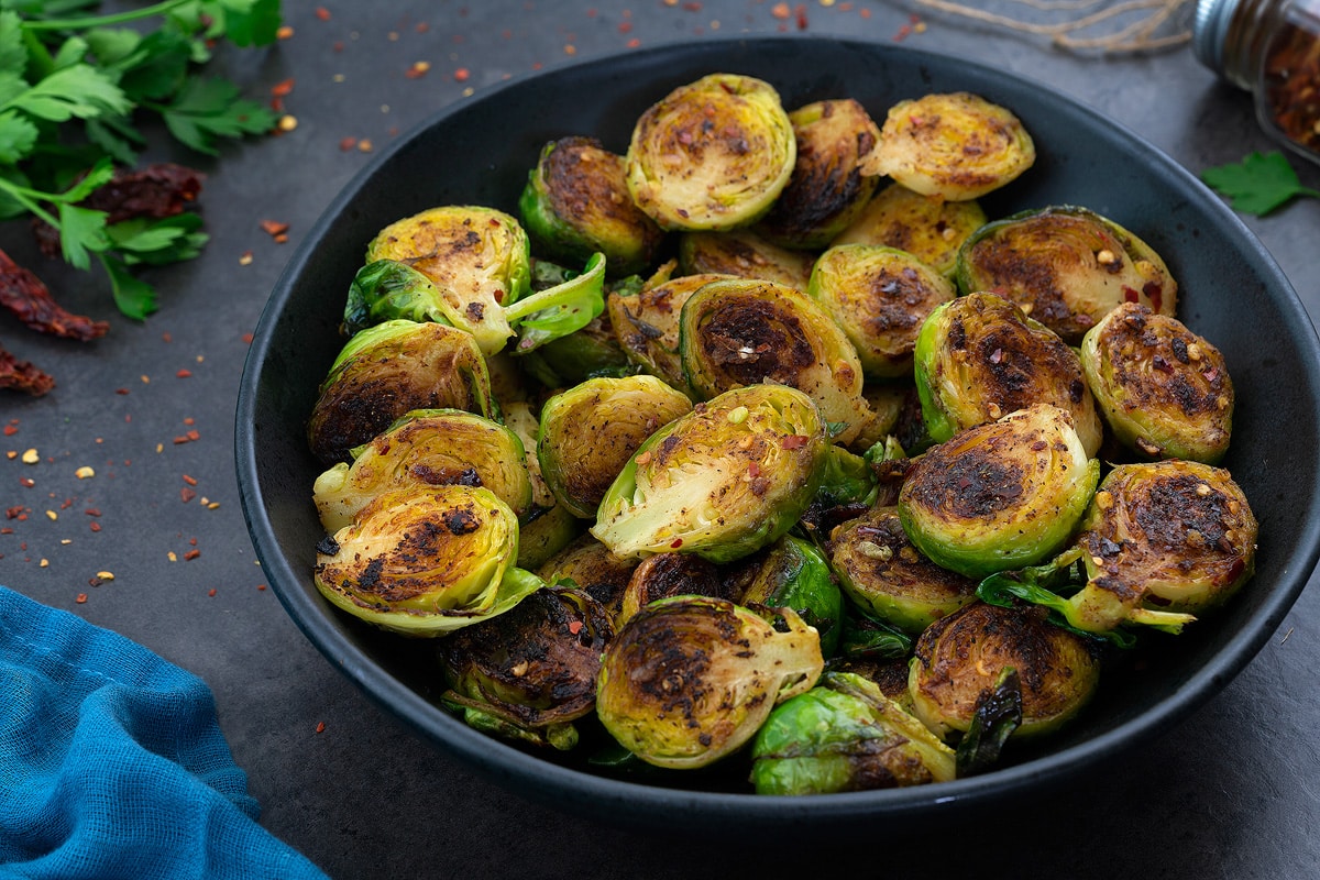 Sauteed Brussel Sprouts in a black bowl with few ingredients scattered around.