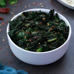 Sauteed Kale in white bowl with few ingredients scattered around.