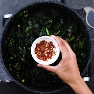 Seasoning the sauteed kale with chili flakes.