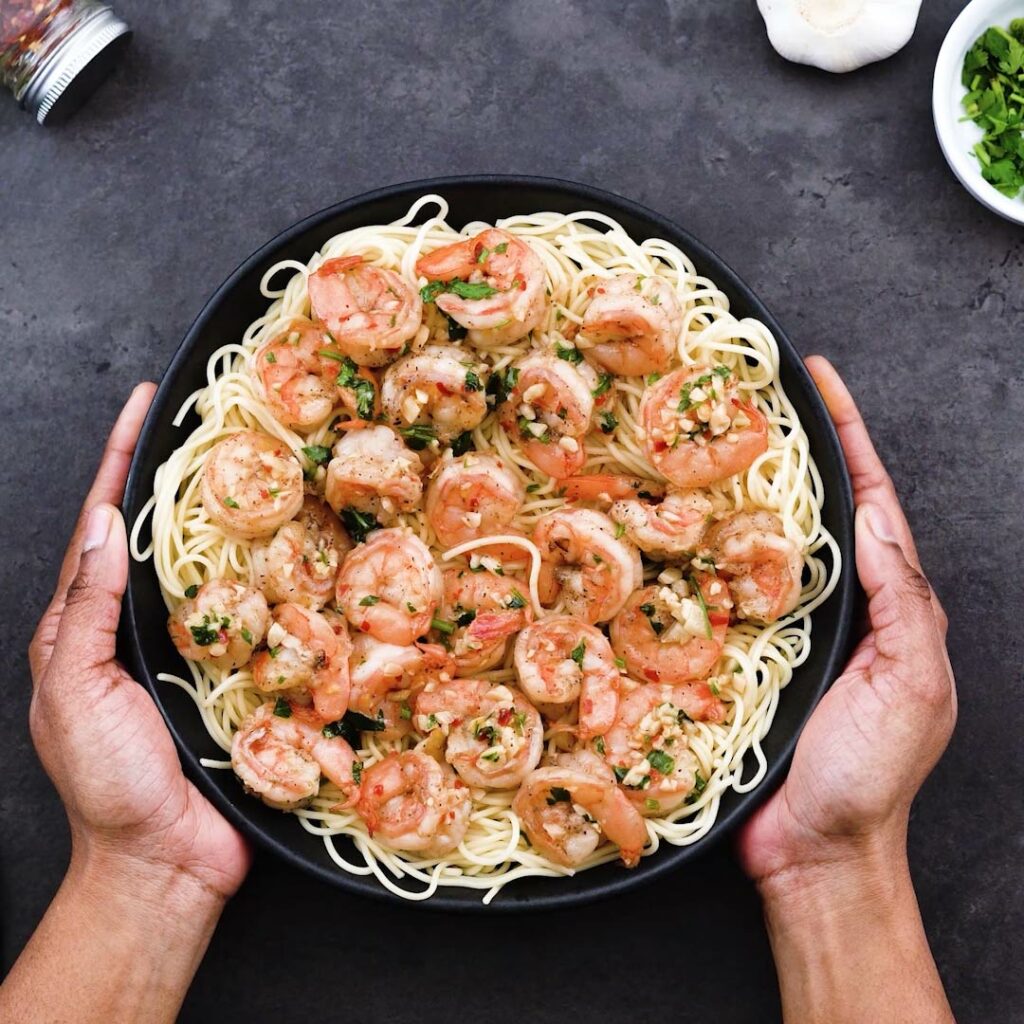 Serving Shrimp Scampi over pasta in a black serving bowl.