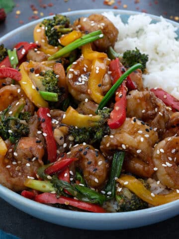 Shrimp Stir Fry served in a bowl with a side of white rice and few ingredients scattered around.