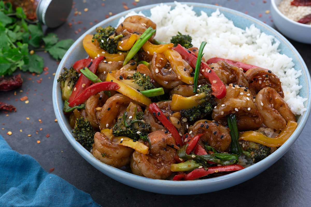 Shrimp Stir Fry served in a bowl with a side of white rice and few ingredients scattered around.