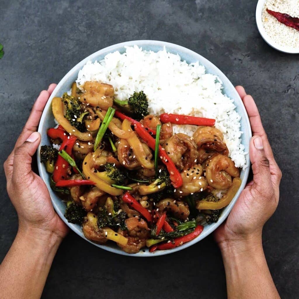 Serving the Shrimp Stir fry over rice on a bowl.