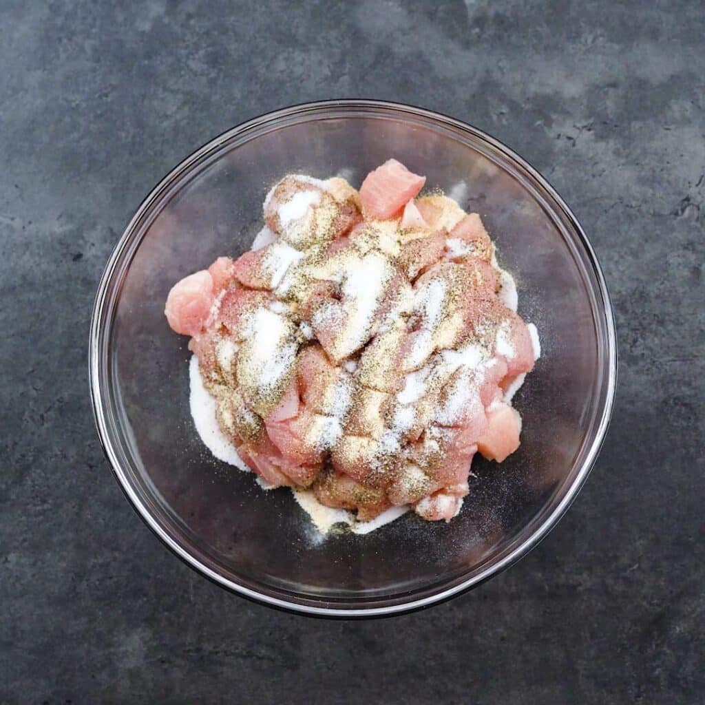 A bowl with chicken pieces with seasoning powders.
