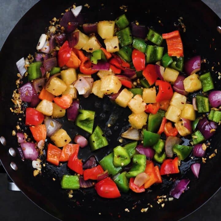 A wok with bell peppers and pineapple along with other aromatics.