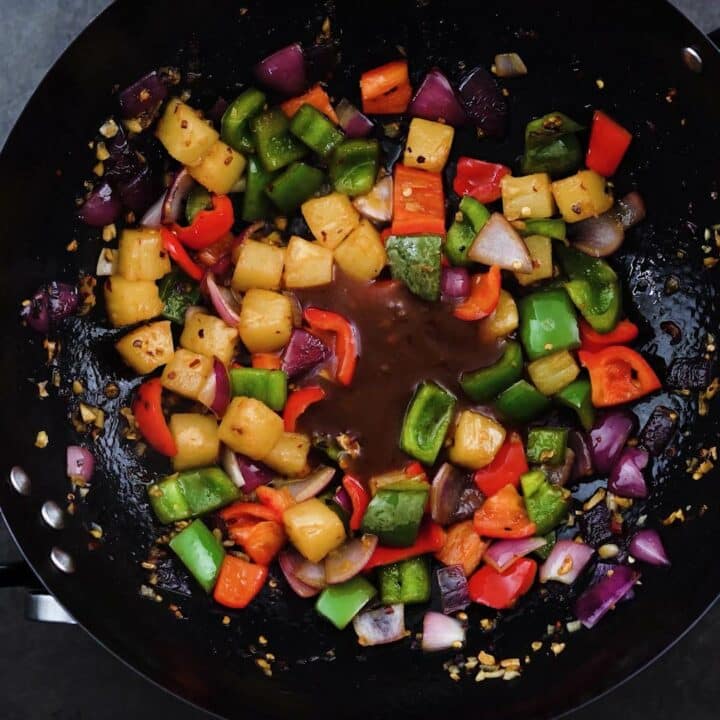 A wok with veggies, pineapple and sweet and sour sauce.