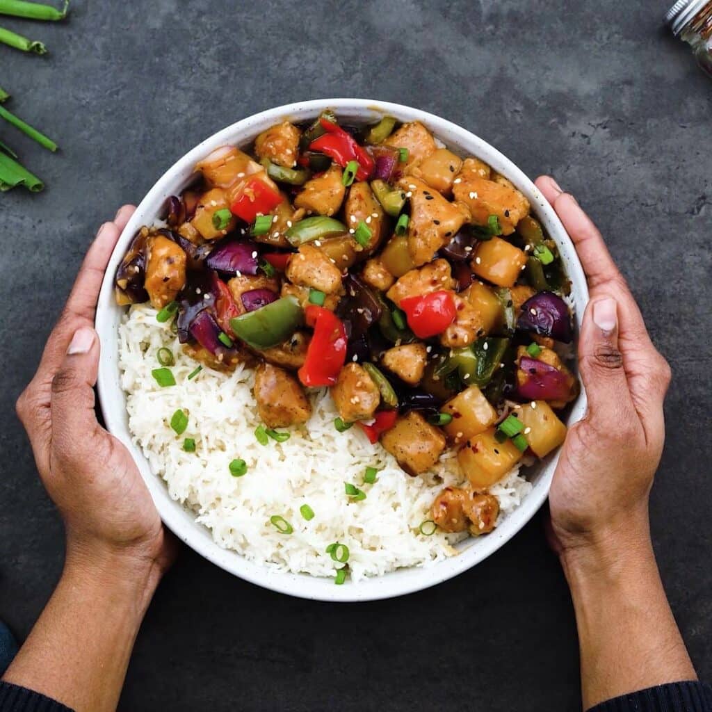 Serving the sweet and sour chicken over white rice in a bowl.