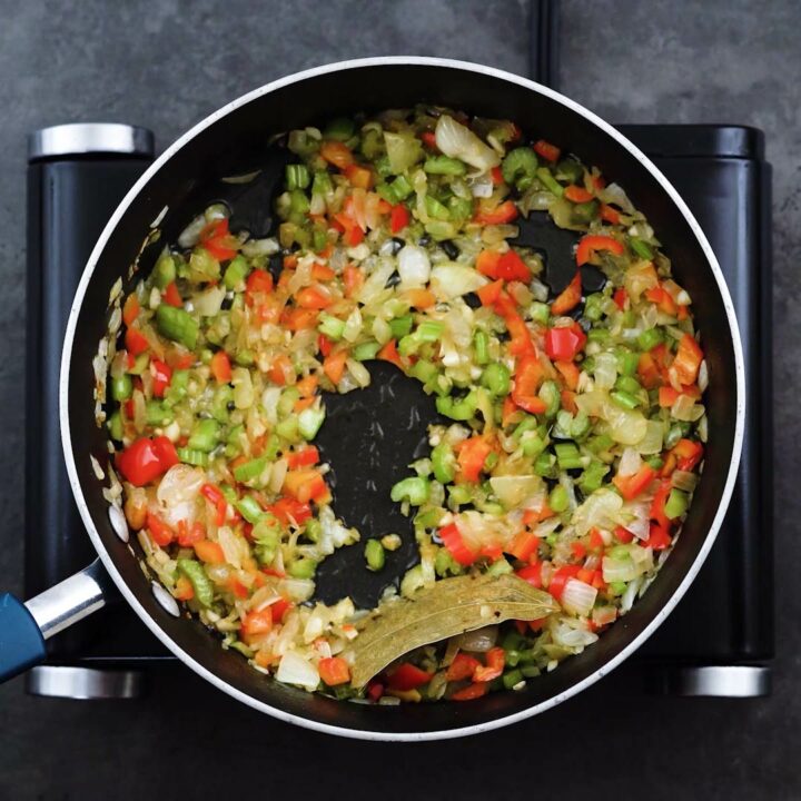 A pan with aromatics, celery and red bell pepper.
