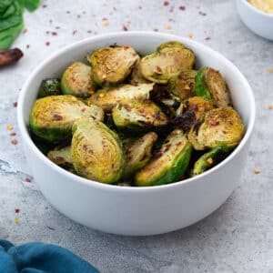 Air Fryer Brussels Sprouts served in a white bowl with few ingredients scattered around.