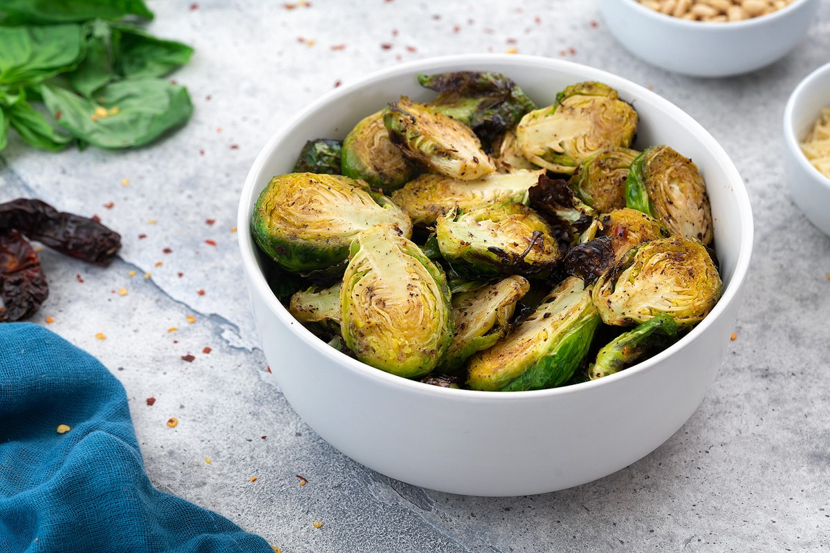 Air Fryer Brussels Sprouts  served in a white bowl with few ingredients scattered around.