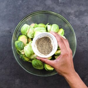 Seasoning the brussels sprouts with black pepper.