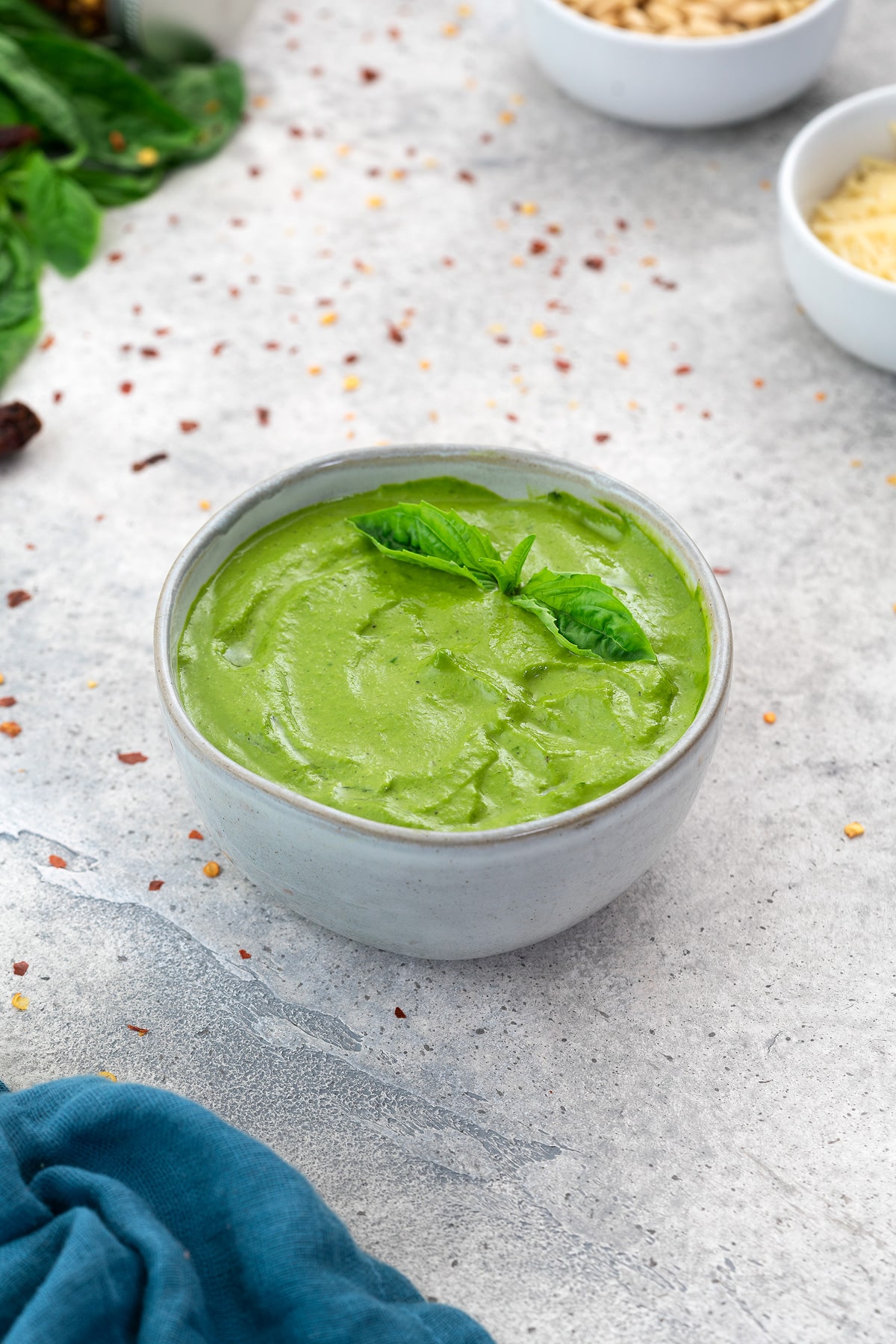 Basil Pesto Sauce in a white bowl with few ingredients scattered around.