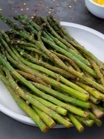 Sautéed Asparagus in a white plate with few ingredients scattered around.