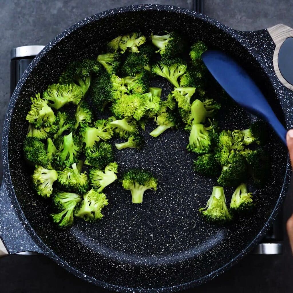 A pan with broccoli that is being stir fried.
