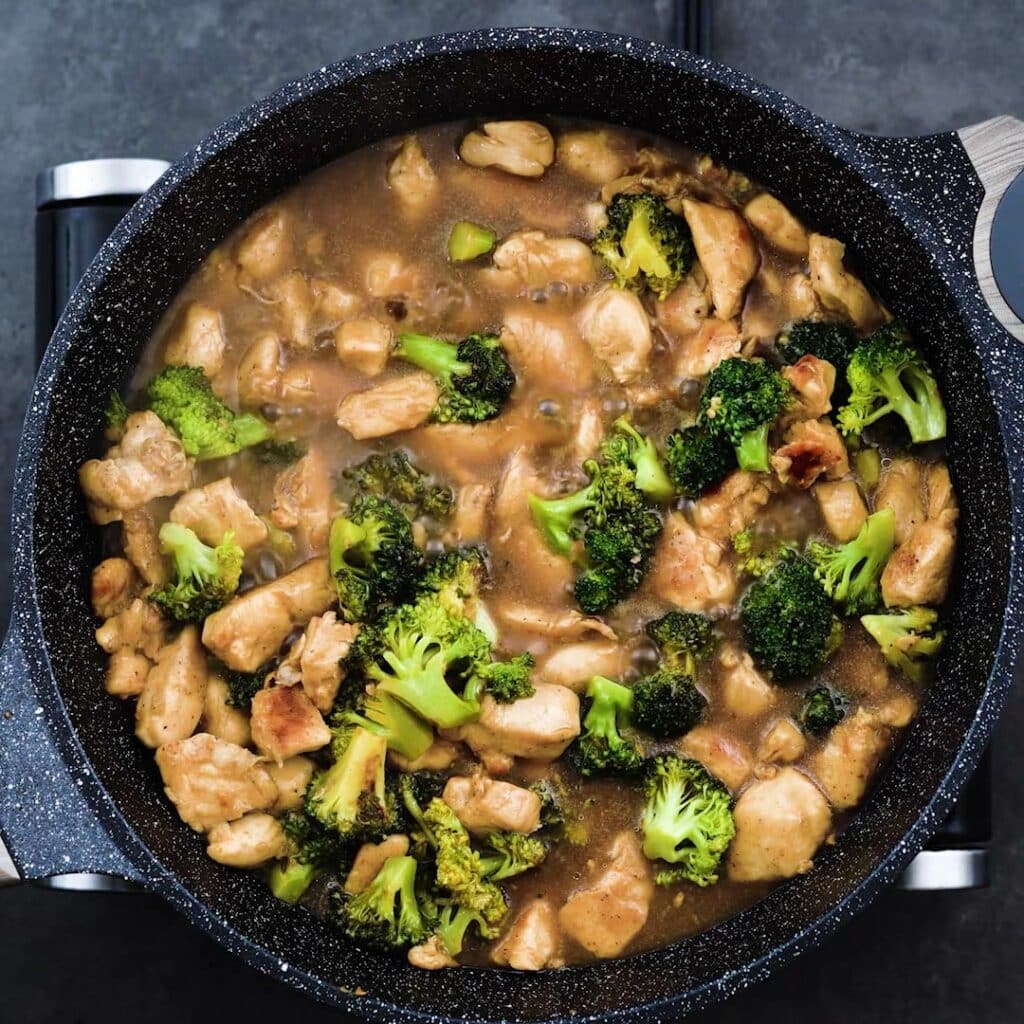 Broccoli and chicken in a stir frying sauce in a pan.