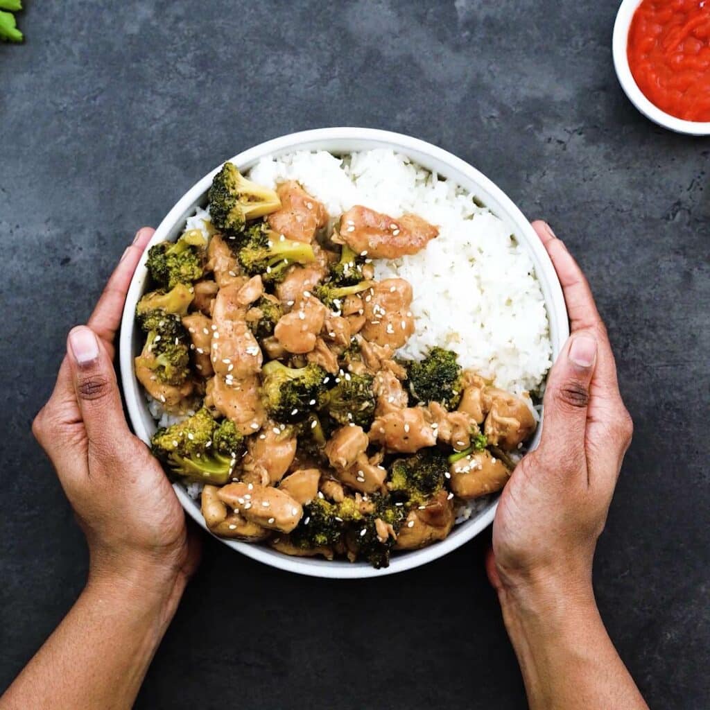 Serving the chicken and broccoli stir fry over rice on a white bowl.