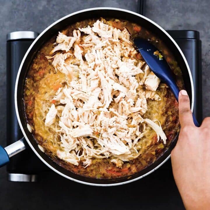 A pan with rice and shredded chicken breast in the soup mix.