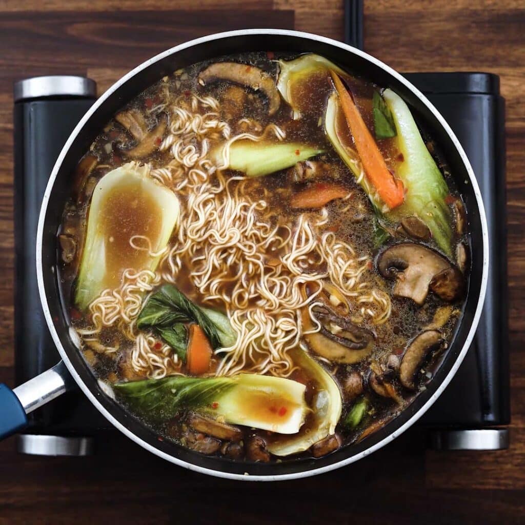 A pan with ramen, broth and veggies.