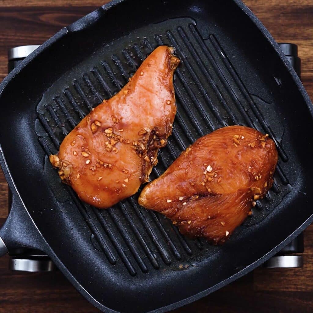 A grill pan with marinated chicken breast.