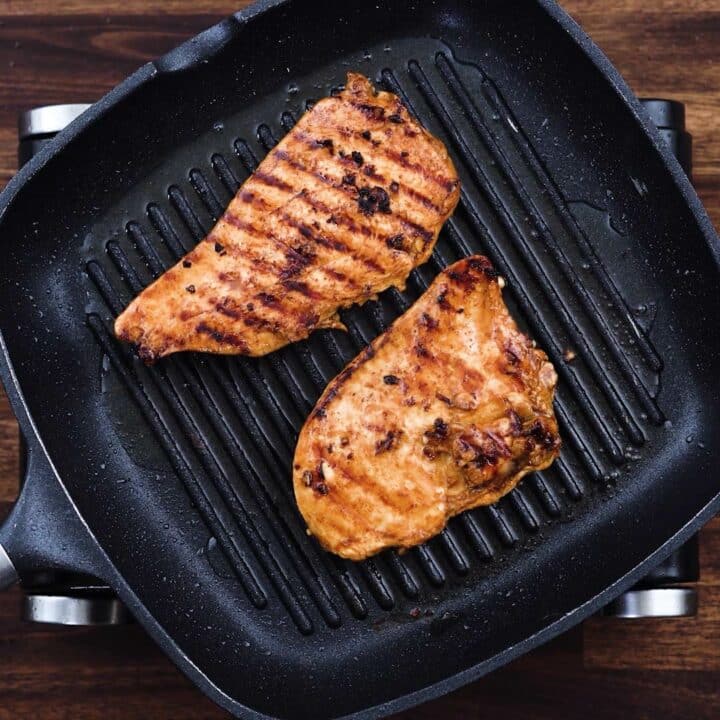A grill pan with chicken breast that is being grilled.