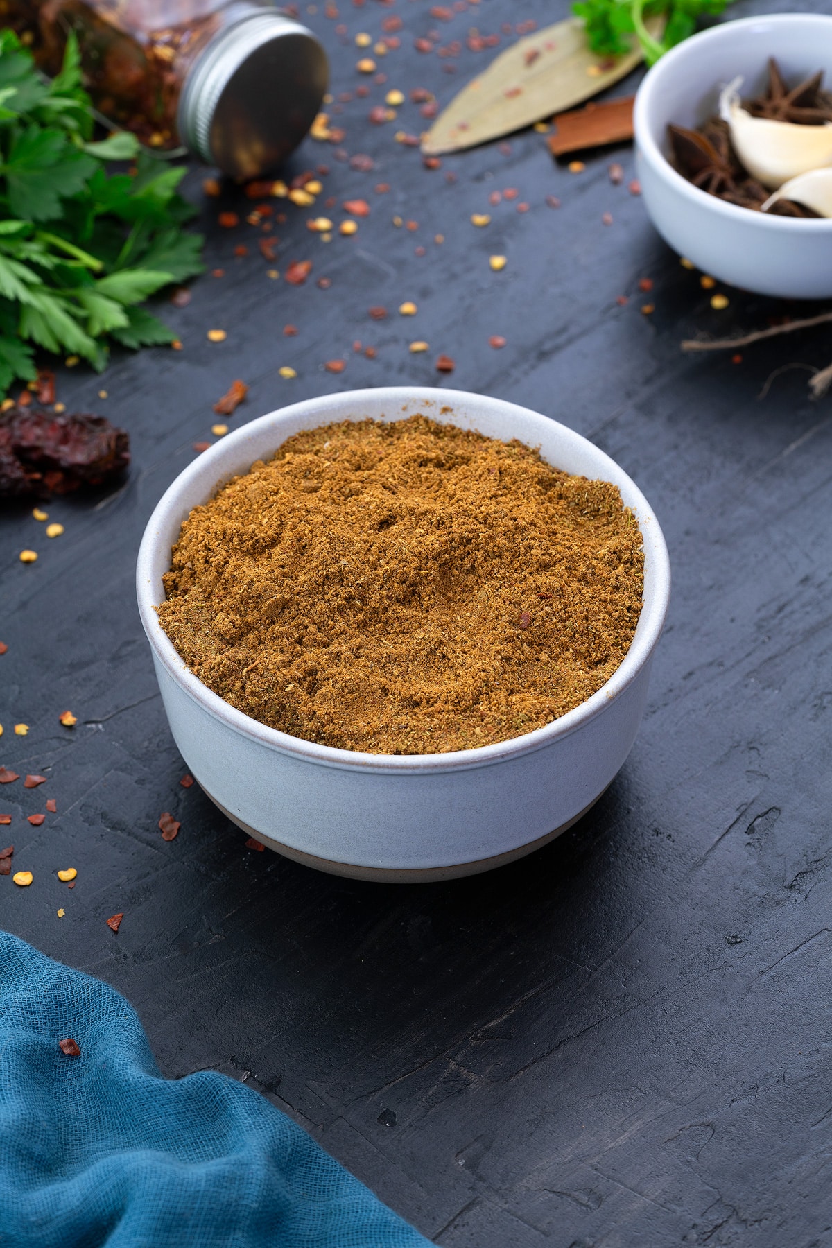 Chinese 5-Spice Powder in a white cup with few ingredients scattered around.