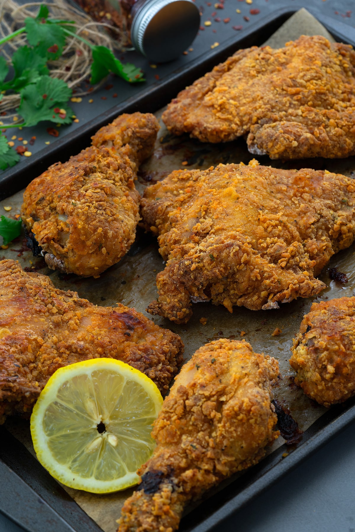 Healthy Oven-Fried Chicken on a baking tray with sliced lemon.