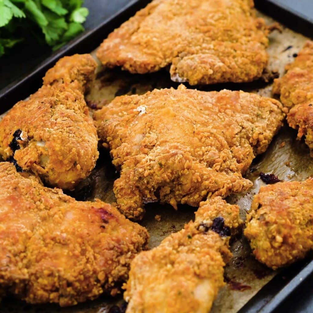 A baking tray with oven fried chicken along with some coriander leaves.
