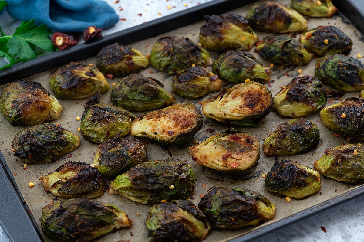 Oven Roasted Brussels Sprouts in a baking tray with few ingredients scattered around.