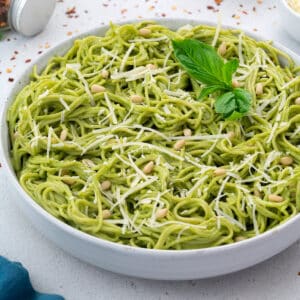 Pesto Pasta in a white bowl with few ingredients scattered around.