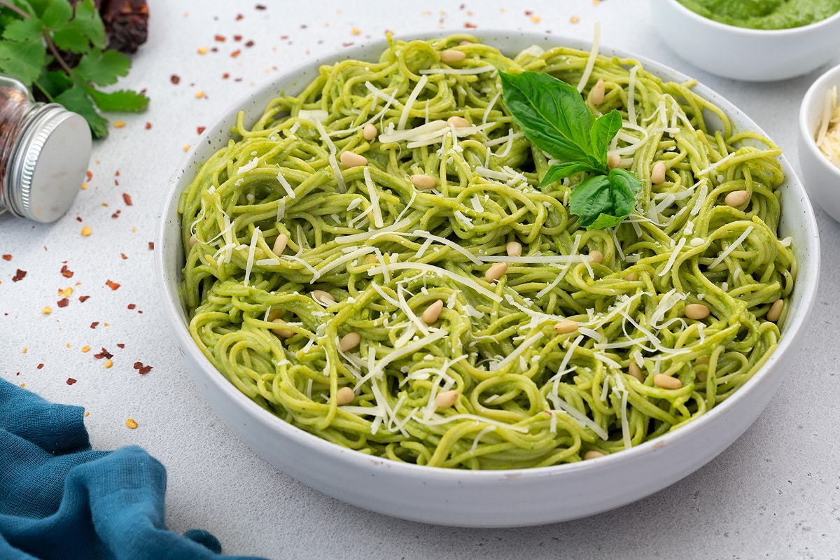 Pesto Pasta in a white bowl with few ingredients scattered around.