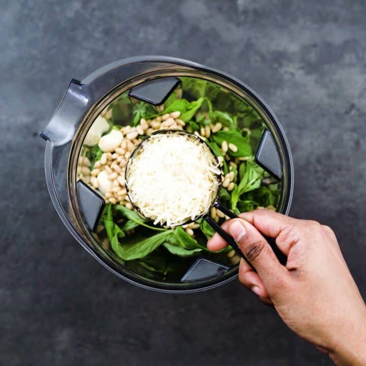 Adding Parmesan cheese to the blender jar with basil.
