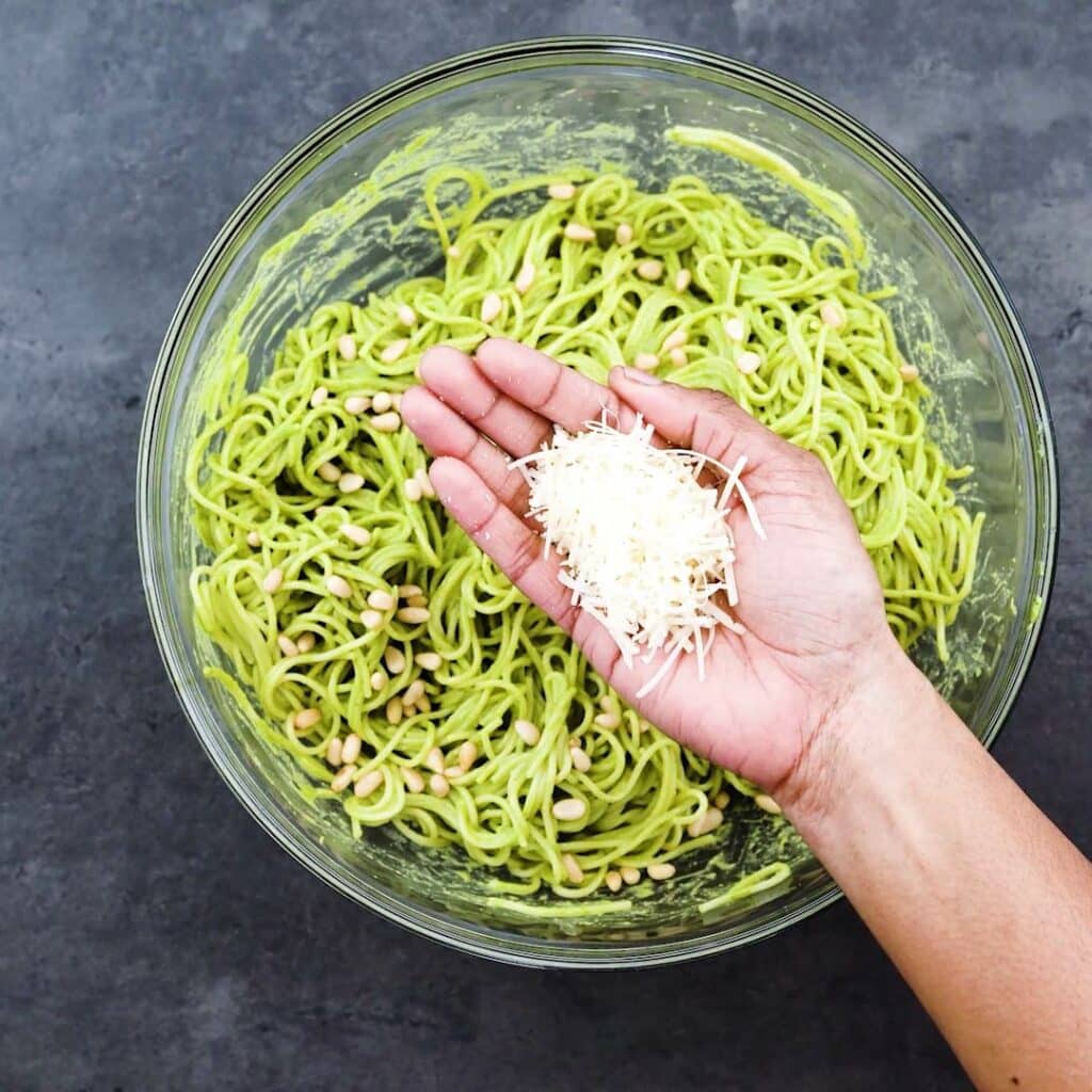 Garnishing pesto pasta with parmesan cheese.