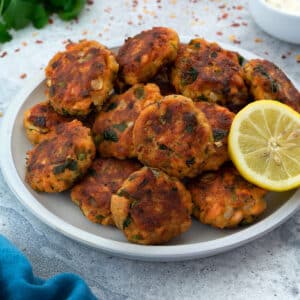 Salmon Patties(cakes) served in a white plate with lemon slice and few ingredients scattered around.