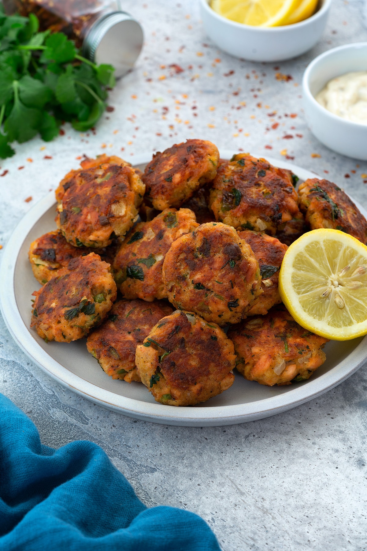Salmon Patties(cakes) served in a white plate with lemon slice and few ingredients scattered around.
