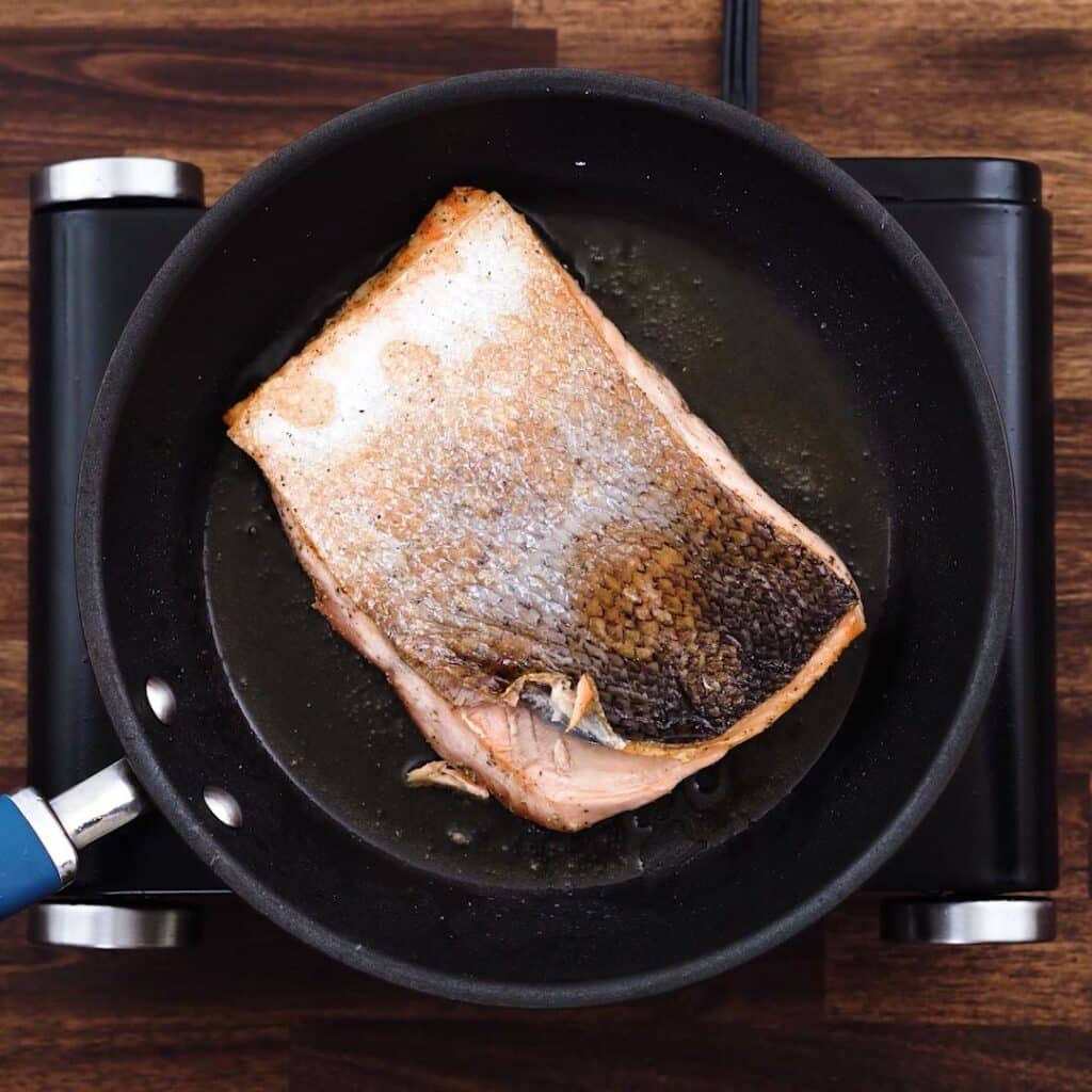 Salmon fillet frying in a pan.