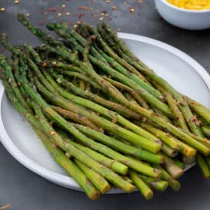 Sauteed Asparagus in white plate with few ingredients placed around.
