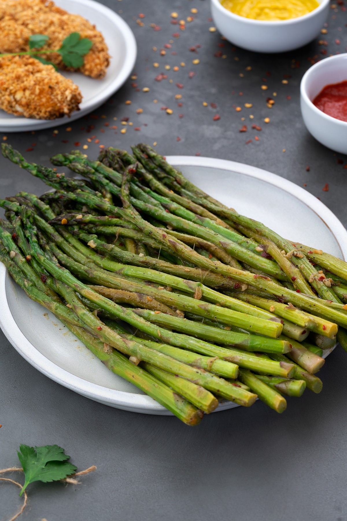 Sauteed Asparagus in white plate with few ingredients placed around.